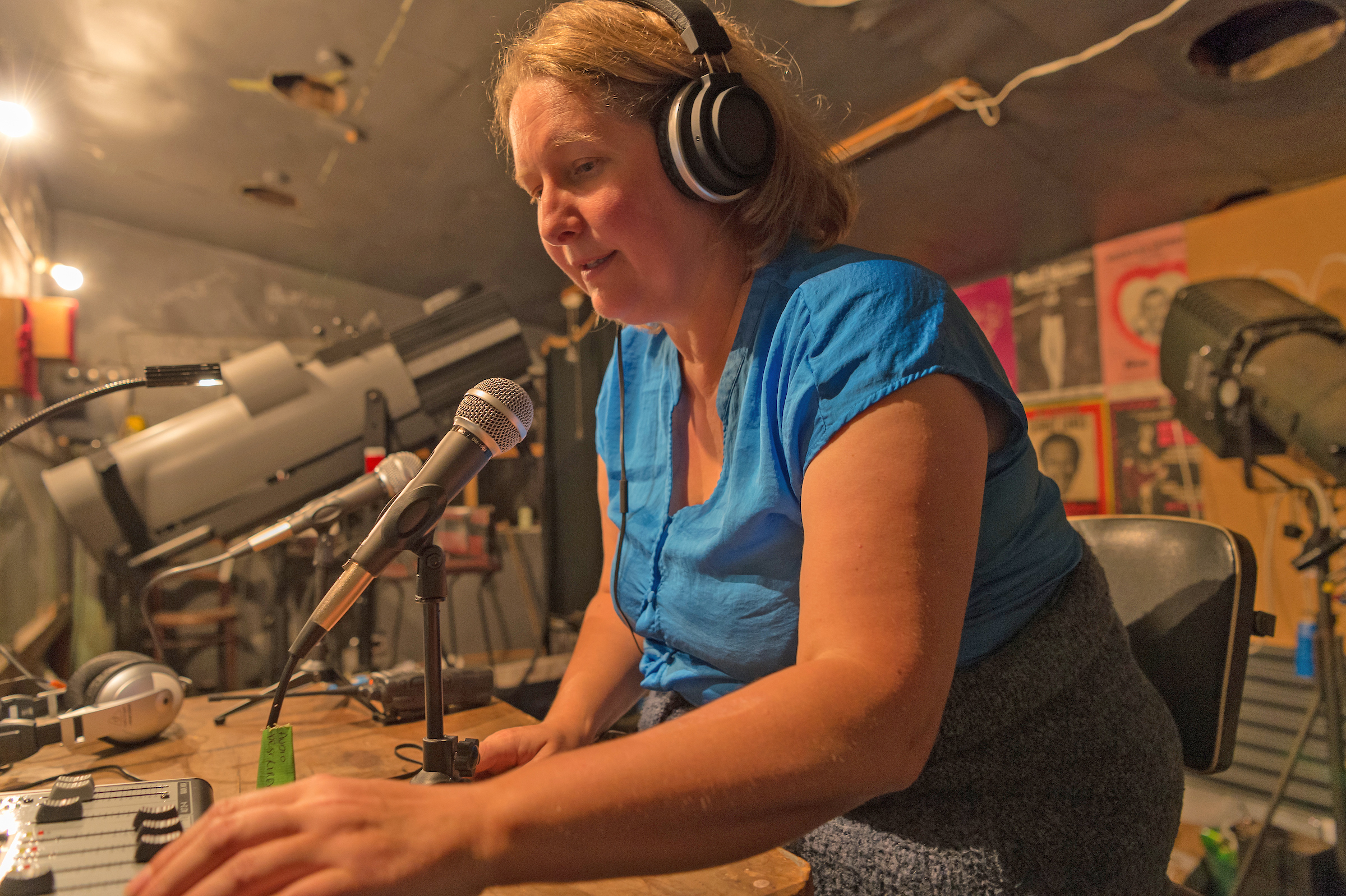 Support Image Nicola Owen sitting in a sound booth speaks into a microphone as she audio describes a performance.